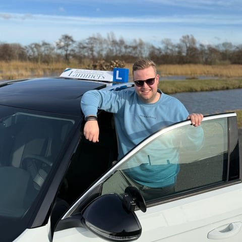 Jordi Lammers leaning out of the door of the white lesson car with the roof sign, laughing
