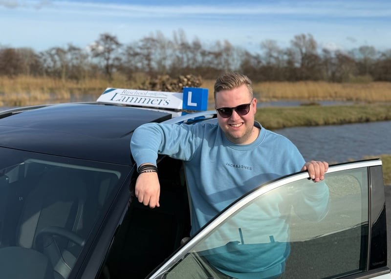 Jordi Lammers leaning out of the door of the white lesson car with the roof sign, laughing
